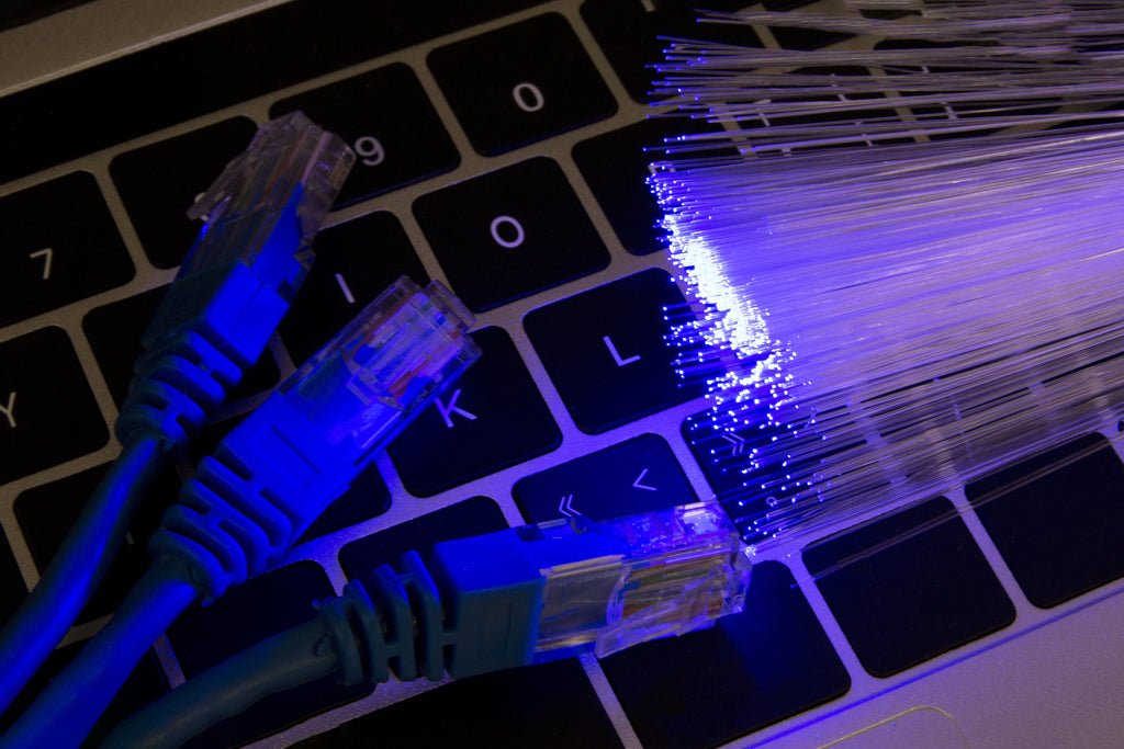 Blaue Ethernet-Kabel und leuchtende Glasfaserstränge liegen auf einer schwarzen Tastatur und betonen die Themen Technologie und Konnektivität. Es geht um das Thema Aktenvernichter und Datenschutz.