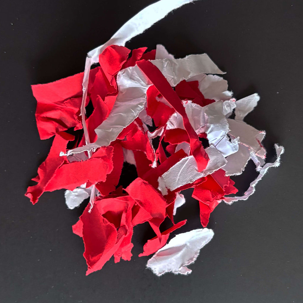 Geshredderte Papierschnipsel in weiß-rot der Sicherheitsstufe P2 - im Zusammenhang mit IDEAL Aktenvernichtern, schlicht vor grauem Hintergrund.