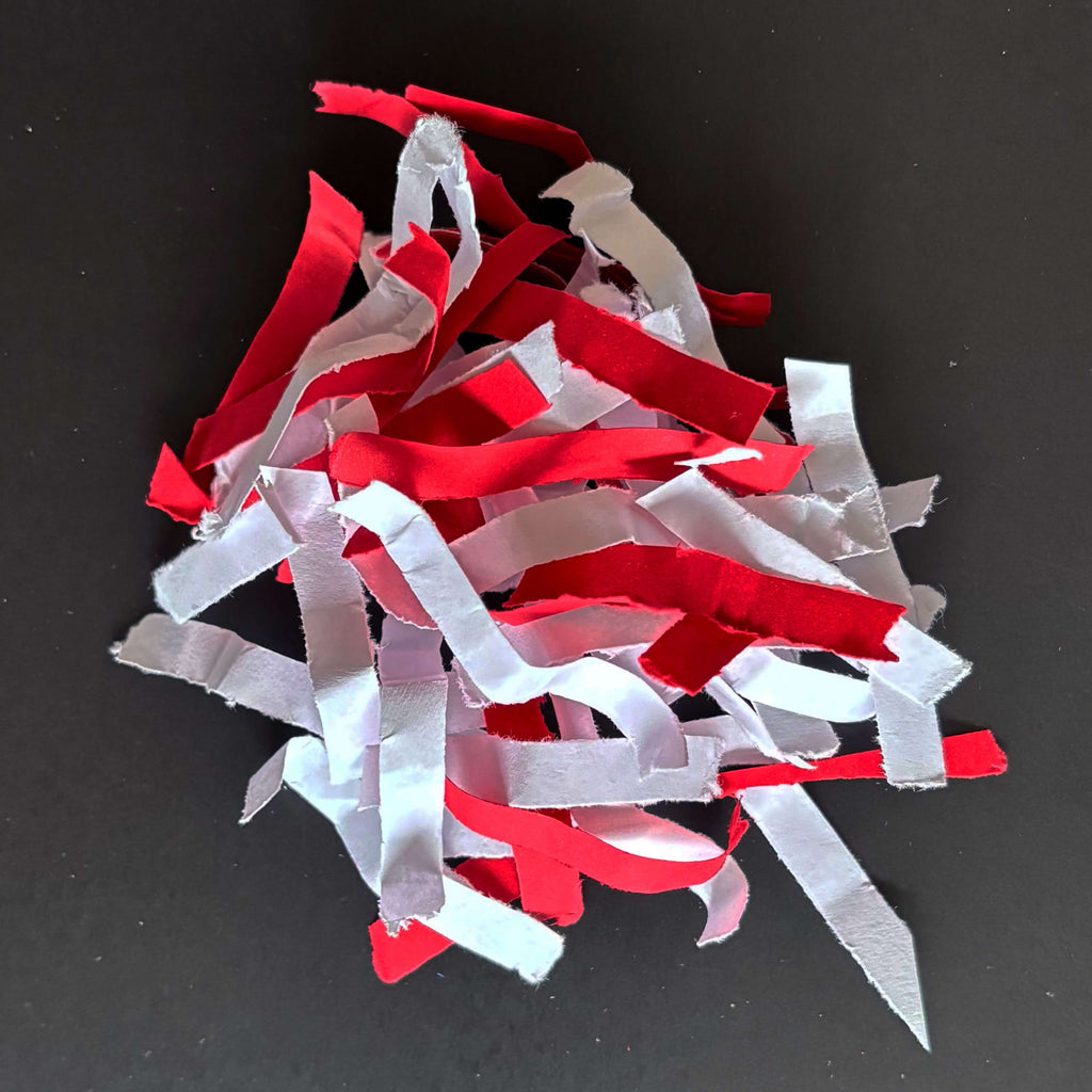 Geshredderte Papierschnipsel in weiß-rot der Sicherheitsstufe P3 - im Zusammenhang mit IDEAL Aktenvernichtern, schlicht vor grauem Hintergrund.