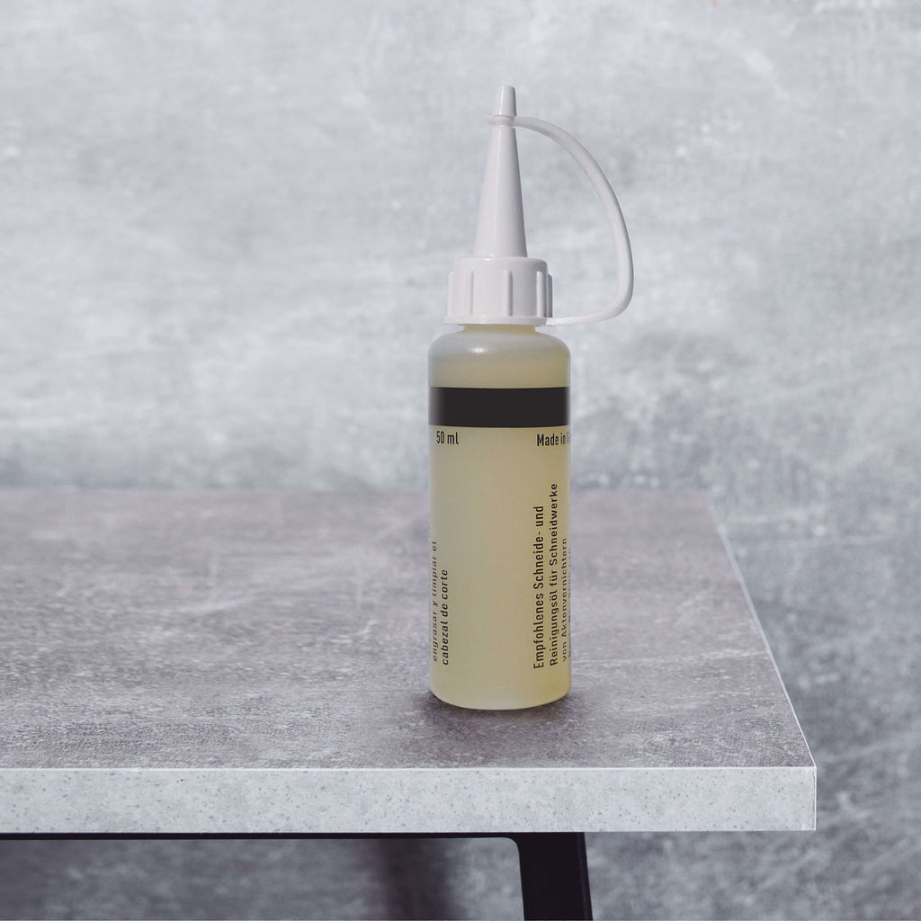 Eine kleine 50-ml-Flasche Spezialöl für IDEAL Aktenvernichter-Schneidwalzen steht auf einem grauen Betontisch vor einem graue, verwischen Hintergrund.