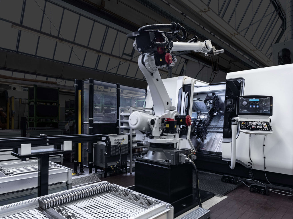 Drehmaschine mit Robotik, montiert auf einem schwarzen Sockel, in einer Fertigungsumgebung.