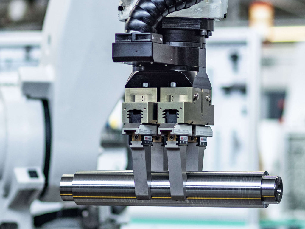 Industrieroboterarm mit einem Greifer, der einen zylindrischen Metallstab hält. 