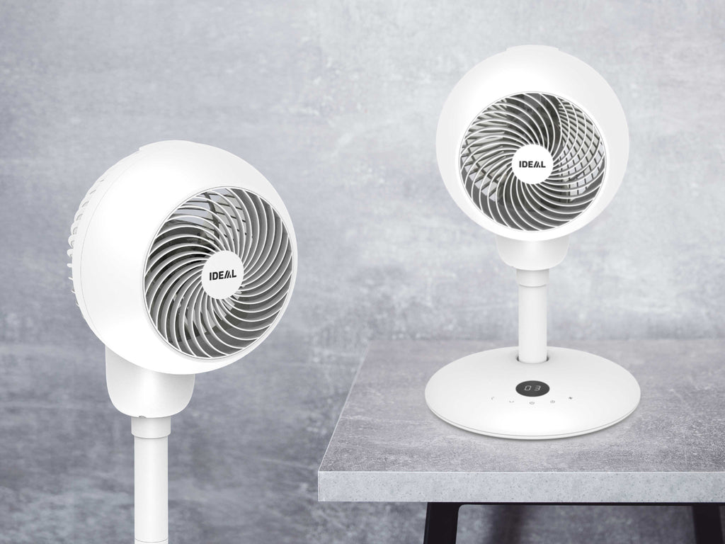 Die weißen Ventilatoren IDEAL FAN1 in zwei Höhen-Optionen vor grauem, verwischtem Hintergrund fotografiert. Einmal als Kurzversion auf einem Tisch, einmal mit Verlängerungs-Stange auf dem Boden.