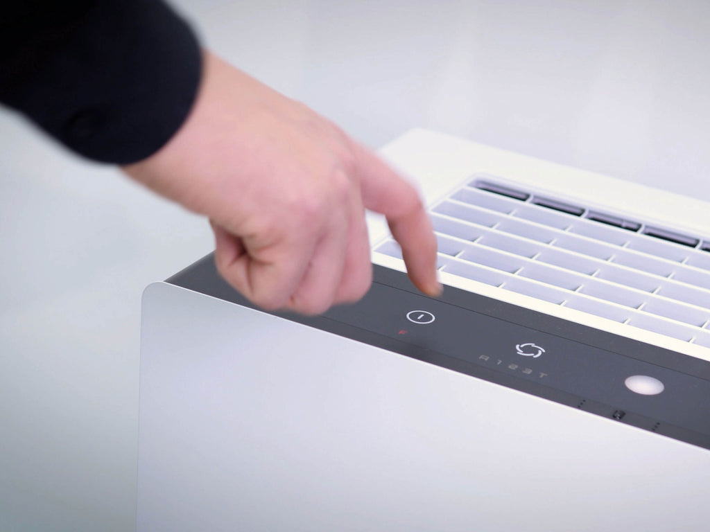 Eine Hand drückt auf die Bedientaste des Luftreinigers IDEAL AP60 PRO, der ausschnitthaft von oben fotografiert wurde.