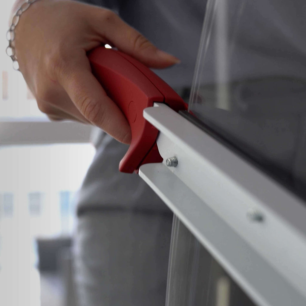Unscharfe Nahaufnahme auf den Ausschnitt einer grau gekleideten Person, die hinter einem IDEAL 1135 Hebelschneider steht. Ihre Hand im Fokus liegende Hand betätigt den roten, ergonomischen Griff des Messerhebels. 