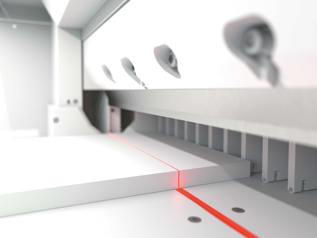 Detailansicht eines IDEAL Stapelschneiders. Zu sehen ist der optische LED-Schnittandeuter: Auf einer Metalloberfläche liegt ein weißer Papierstapel, darüber ist das Stapelschneider-Messer, auf dem Papierstapel verläuft eine rote Licht-Sichtlinie. Hinter dem Papier ist der rechenartige Rückanschlag zu sehen.