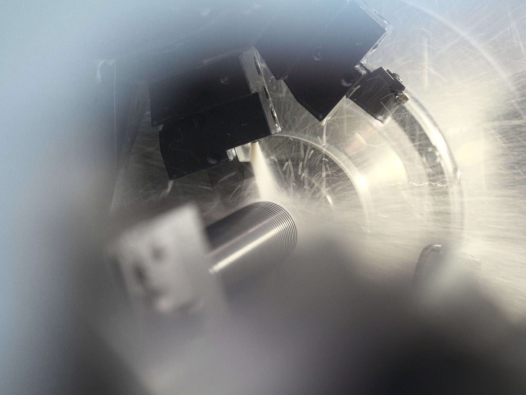 Metallzylinder wird in einer Maschine bearbeitet, umgeben von mechanischen Bauteilen und Lichtreflexionen.