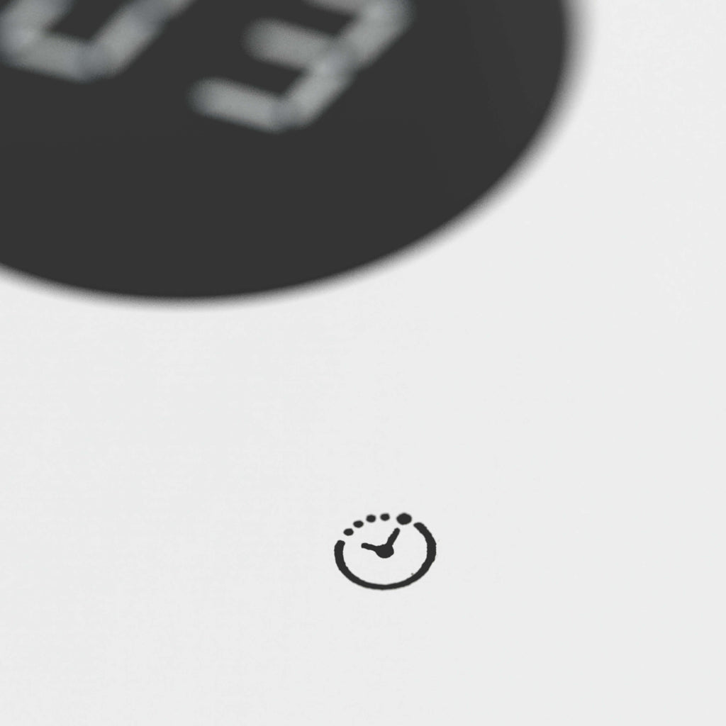 Nahaufnahme auf ein Uhr-Icon beim Ventilator IDEAL FAN1, das die Timer-Funktion symbolisiert. Links oben angeschnitten ein rundes Display, unscharf eine Zahl 03 dargestellt.