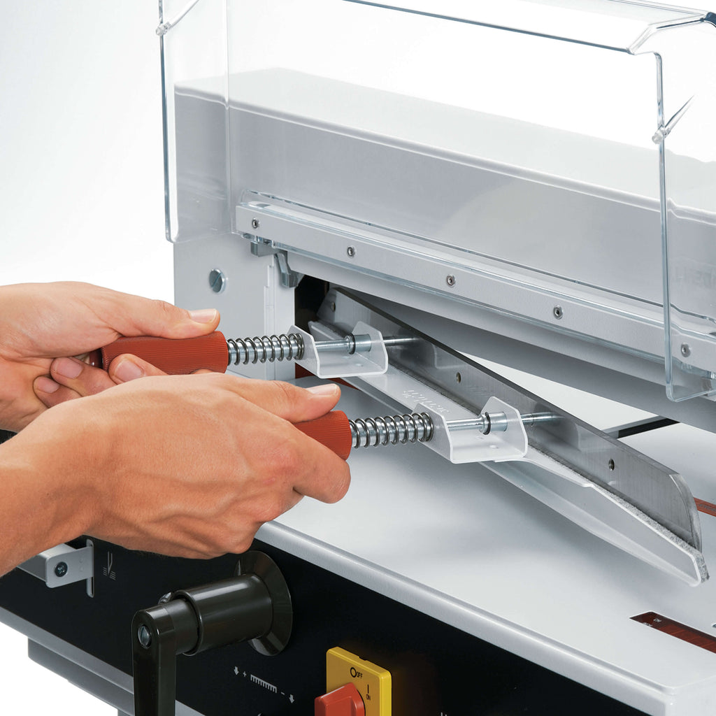 Nahaufnahme eines sicheren Messerwechsels bei einem IDEAL Stapelschneider 4315 oder 4350. Zwei Hände halten ein Werkzeug mit dem Stapelschneider-Messer. Die Hände sind geschützt. Man sieht noch einen Teil der Sicherheitshaube und das Bedienpanel der Maschine.