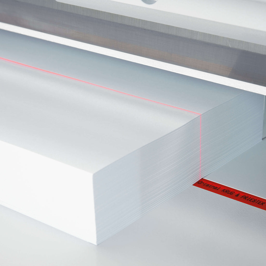 Detailansicht eines IDEAL Stapelschneiders. Zu sehen ist der optische LED-Schnittandeuter: Auf einer Metalloberfläche liegt ein weißer Papierstapel, darauf verläuft eine rote Licht-Sichtlinie.