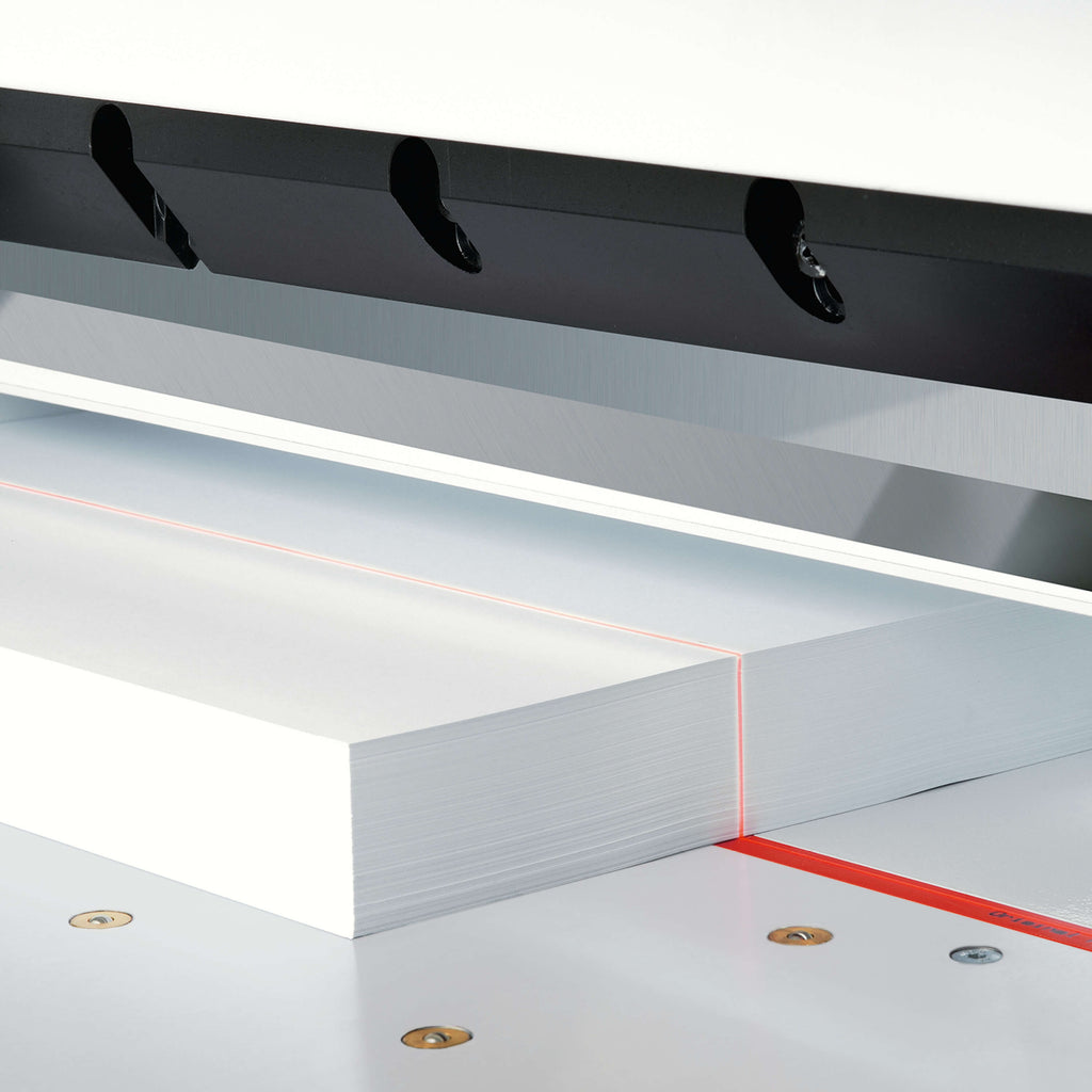 Detailansicht eines IDEAL Stapelschneiders 7260 LT. Zu sehen ist der optische LED-Schnittandeuter: Auf einer Metalloberfläche liegt ein weißer Papierstapel, darauf verläuft eine rote Licht-Sichtlinie.