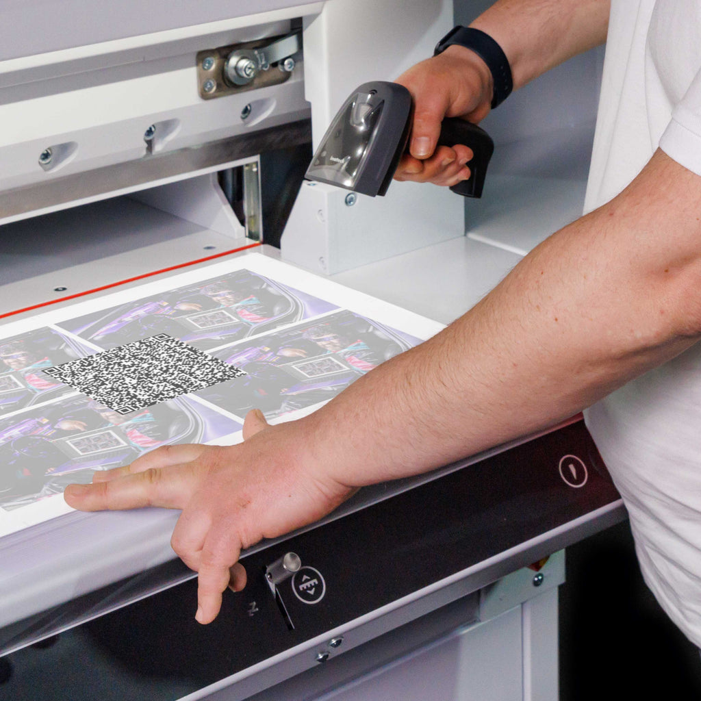 Ein Mann hält einen Scanner über einen futuristischen Schnittbogen an einem programmierbaren Stapelschneider IDEAL THE56 oder THE68, der mit der Automatisierungs-Software Speedcut arbeitet, um eine einfache Datenübertragung vom Schnittbogen zur Maschine zu ermöglichen.