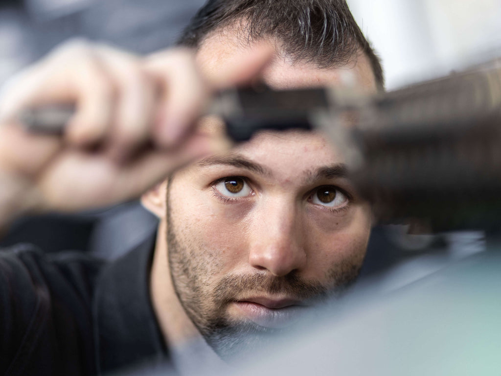 Ein Arbeiter kontrolliert eine Messerwelle mit einem Messschieber. Er trägt ein schwarzes Oberteil und wirkt dabei hochkonzentriert