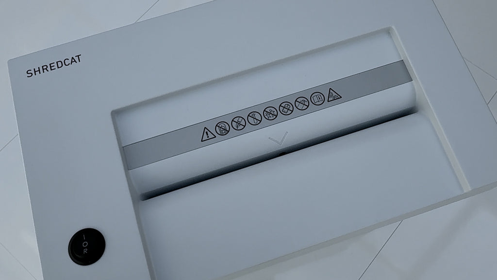 Vorschaltbild zum Video mit der Geräteoberseite des Aktenvernichters IDEAL Shredcat 8200. Zu sehen sind der Ein-Aus-Rückwärts-Schalter und die Zuführöffnung mit diversen Warn-Icons. Links oben der Schriftzug SHREDCAT.