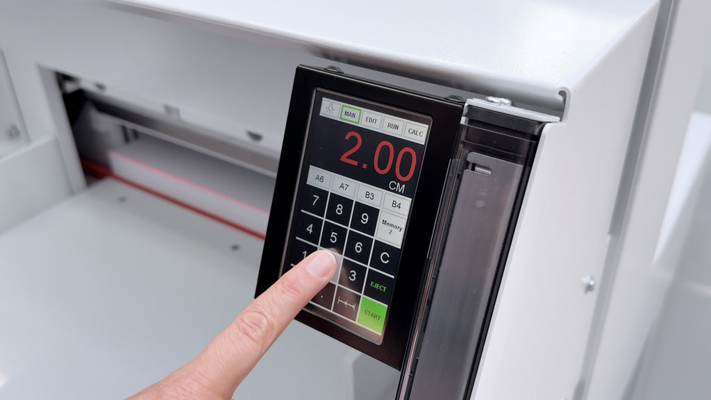 Szenenbild aus dem Video zum Schnittvorgang des elektrischen Stapelschneiders IDEAL 4855: Nahaufnahme des digitalen Touchpads, auf dem der Zeigefinger einer Hand gerade ein Maß eingibt.