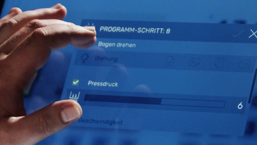 Szenenbild aus dem Bedien-Video des programmierbaren Stapelschneiders IDEAL THE56 mit Zoom auf eine Hand, die den Anpressdruck in der komfortablen Bedienoberfläche des großen 15,6“-Touchmonitors justiert.